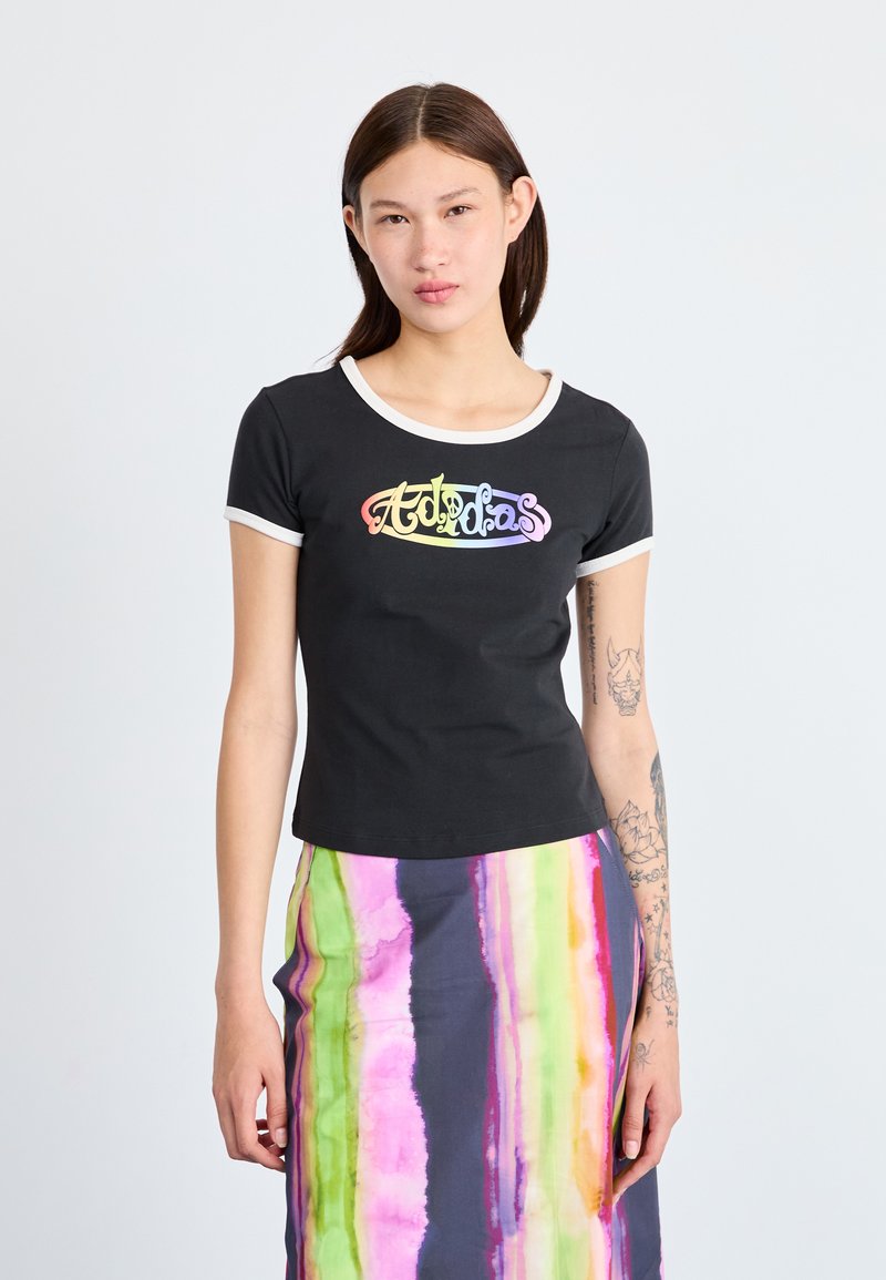 Sort T-shirt med korte ærmer og en hvid rund halsudskæring, med et flerfarvet "Adidas" logo. Sammen med en flerfarvet stribet nederdel.