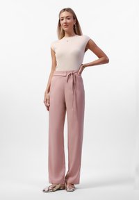 Lichtbeige fitted top met korte kapmouwen, gecombineerd met hooggesneden, zachtroze wijde broek en metallic balletschoenen.