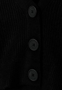 Cardigan en maille côtelée noire avec quatre boutons noirs le long de la patte de boutonnage, et un fini en tissu texturé.