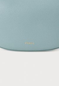 Ljusblå läderhandväska med texturerad yta och en guldfärgad "FURLA"-logotyp präglad på framsidan, med en slät kontur.