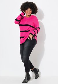 Suéter rosa brillante con rayas horizontales negras, combinado con leggins negros que presentan paneles texturizados y botas negras con tachuelas.