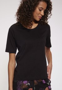 Camiseta negra de manga corta hecha de algodón suave con un clásico cuello redondo. Combinada con pantalones florales estampados, que presentan colores vibrantes.
