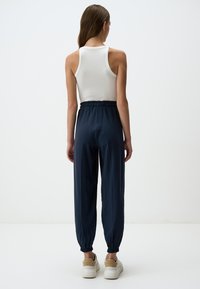 Marineblauwe tapered joggers met elastische boorden en een trekkoord in de taille, gecombineerd met een aansluitend wit geribbeld tanktop. Glad stoftextuur.