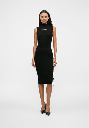 Rochie midi neagră, cu dungi, având decolteu înalt, detaliu cu șireturi pe lateral și accent cu logo pe piept, asortată cu pantofi cu toc ascuțit negri.