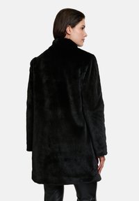 Black faux fur coat with a high collar, long sleeves, and a loose fit, featuring a soft, textured surface and mid-thigh length.