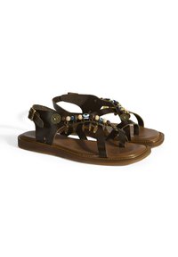 Braune Ledersandalen mit flacher Sohle, verziert mit kunstvollen Perlen- und Charmdetails am Riemen sowie einem verstellbaren Knöchelverschluss.