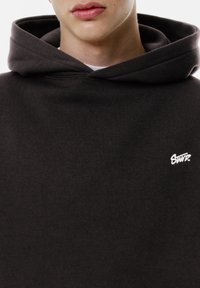 Dunkelgrauer Hoodie aus weichem Material, mit einer großen Kapuze und einem kleinen weißen Logo auf der Brust, mit nahtlosem Design.