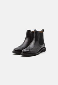 Bottes Chelsea en cuir noir avec une finition brillante, motif brogue détaillé, panneaux latéraux élastiques et un talon bas empilé.