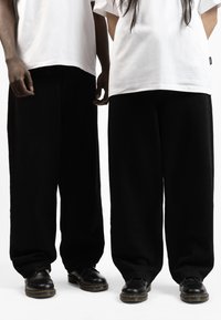 Black wide-leg trousers made from a soft fabric, paired with plain white t-shirts. Black shoes with yellow stitching complete the look.