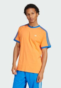 Camiseta de manga corta naranja con acentos azules, con un cuello redondo y un logo blanco en el pecho. Hecha de material de algodón suave.