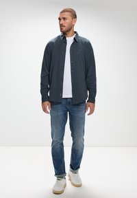 Knapp-up skjorta i mörk marinblå, kombinerad med vit t-shirt, blå jeans och vita sneakers. Har en avslappnad design och en ledig passform.