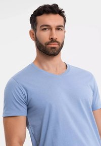 Světle modré tričko s výstřihem do V vyrobené z jemné tkaniny. Krátké rukávy s čistým zakončením a bez viditelných log nebo vzorů.