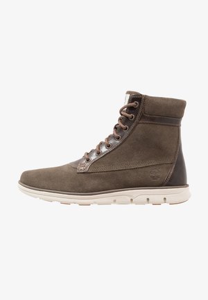 Botín de ante y cuero marrón con cordones, cuello acolchado y suela de goma blanca, vista lateral, logotipo de Timberland en el talón.