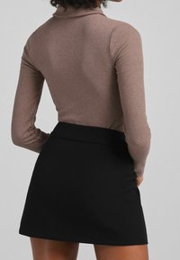 Ribbad, långärmad, taupe topp i kombination med en svart, figurnära mini-kjol som visar en slät textur och välsittande design.