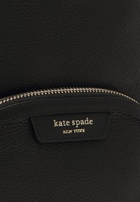 Zwarte leren rugzak met een gestructureerde afwerking, voorzien van een gouden rits en een label met de tekst "kate spade NEW YORK" in gouden letters.