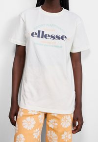 Weißes Baumwoll-T-Shirt mit rundem Halsausschnitt, ausgestattet mit einem mehrfarbigen Textdesign: "ellesse"-Logo und italienischen Phrasen. Lockere Passform.