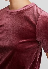 Burgunderröd sammet t-shirt med en slät textur, rund halsringning och korta ärmar, med subtil lyster och detaljer vid sidsömmen.