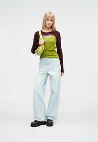 Μπλούζα μακρυμάνικη με διαχωρισμό χρωμάτων, με πράσινο κορμό και μπορντό μανίκια, συνδυασμένη με ανοιχτό μπλε τζιν παντελόνι φαρδιάς γραμμής και μαύρα παπούτσια με πλατφόρμα.