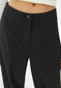 Černé dobře padnoucí kalhoty s hladkou texturou, s předním zapínáním na knoflík, bočními kapsami a přiléhavým pasem.
