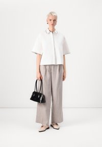 Camicia bianca corta con bordo nero a contrasto, pantaloni larghi a righe grigio chiaro, borsa nera e scarpe basse chiare.