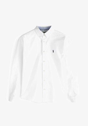 Balta ilga piedurkņu krekls, izgatavots no kokvilnas, ar pogām aizveramu kaklu, priekšējo plati ar pogām un mazu tumši zilu omāru emblēmu uz krūtīm.