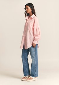 Light pink striped oversized shirt with a collar, single pocket, and balloon sleeves, paired with blue wide-leg jeans and beige platform sandals.