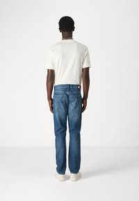 Camiseta blanca de manga corta y jeans de mezclilla azules de corte recto, con bolsillos traseros y una etiqueta con el logo en la cinturilla.