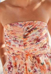 Ziedu strapless kleita ar pleitu dizainu. Krāsas ietver persiku, violetu un oranžu, ar mīkstu, vieglu audumu.