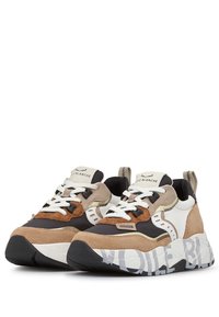 Zapatillas gruesas que presentan una mezcla de gamuza beige, marrón y negra, con materiales de malla y goma; cordones blancos prominentes y suela con patrón.