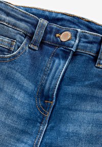Blå denimjeans med dragkedja och knappstängning, med kontrasterande orange sömmar och klassisk femfickorsdesign.