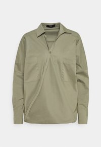 Camicia verde oliva in cotone, con chiusura a bottoni, due tasche frontali e un design a taglio diagonale con maniche lunghe.