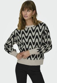 Maglione a zigzag nero e crema con maniche lunghe, scollatura rotonda e polsini e orlo a coste, realizzato in morbido tessuto lavorato a maglia.