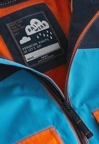Färgglad regnjacka med en svart etikett som säger "RAIN WEAR", orange fleece-foder och en blå utsida med en dragkedja i mitten.