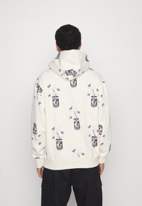 Felpa bianca con grafica floreale e patch in multicolor, cappuccio, polsini e orlo a coste, realizzata in morbido tessuto di cotone.