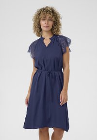 Navy blue dress with lace sleeves, a V-neck, and a drawstring waist. Smooth texture, knee-length design with side slits.