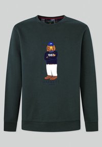 Sudadera verde oscuro hecha de algodón, con un gran perro bordado con una gorra y el texto "1983" y "Hackett London" debajo. Diseño clásico.