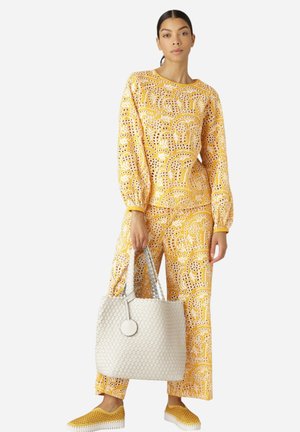 Geel gestippelde twee-delige outfit met oogjesdetails, vergezeld van een witte geweven tote bag en gele instappers met perforaties.