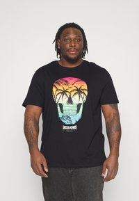 Black cotton t-shirt featuring a colorful skull graphic with palm trees and sunset hues of pink, orange, and blue. Brand text included.