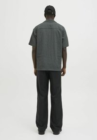 Camisa gris de manga corta con textura, combinada con pantalones anchos negros y una gorra de béisbol negra, vista desde atrás.