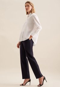 Hvid skjorte med lange ærmer og knappet krave, kombineret med mørkeblå, lige bukser og sorte sandaler med høje hæle.