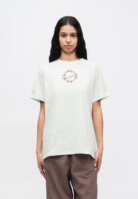 Svetlosivé bavlnené tričko voľného strihu s centrálnym kruhovým grafickým motívom obsahujúcim švih a kvetinové ozdoby. Krátke rukávy.