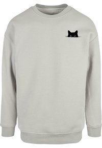 Sudadera gris clara hecha de un tejido suave, que presenta un pequeño gráfico de un gato negro con ojos grandes en el lado izquierdo del pecho. Puños y dobladillo de canalé.