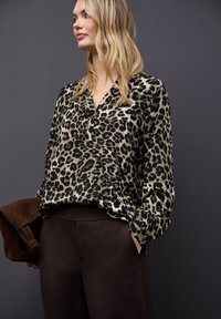 Halenka s leopardím vzorem z lehkého materiálu, s dlouhými rukávy a výstřihem do V. V kombinaci s tmavě hnědými kalhotami a hnědou semišovou kabelkou.