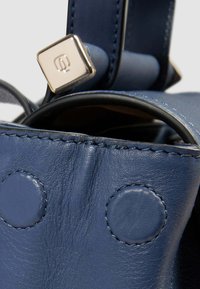 Borsa in pelle blu con cuciture visibili, dettaglio hardware arrotondato e texture liscia. Presenta abbellimenti circolari sulla superficie.