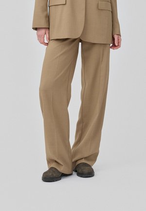 Pantalones tailored de color marrón claro con un diseño de pierna ancha, fabricados en tejido texturizado, combinados con calzado oscuro. Un look sencillo y estructurado.