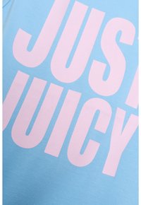T-shirt di cotone azzurro chiaro con grande e audace testo rosa che recita "JUST JUICY" sulla parte anteriore. Texture liscia, scollo rotondo.