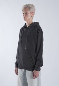 Sötétszürke kapucnis pulóver kenguruzsebekkel, húzózsinórral a nyaknál és bordázott mandzsettával. Világoskék, laza szabású farmernadrággal kombinálva.