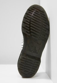 Černá gumová podešev s texturovaným vzorem pro lepší grip a vystouplým logem. Vyjímatelný design, vhodný pro různé povrchy.