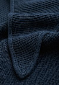 Marineblauwe gebreide stof met een geribbelde textuur, voorzien van een gladde, gevouwen rand. Dikke garen met zichtbare stikdetails.