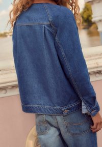 Kurtka dżinsowa o luźnym kroju, z lekkimi przetarciami na mankietach, w niebieskim odcieniu i widocznym szwie. W zestawie z pasującymi dżinsami.